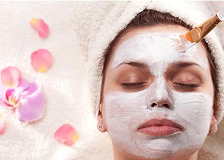 Women receiving a facial mask, eyes closed while laying on table with flower petals